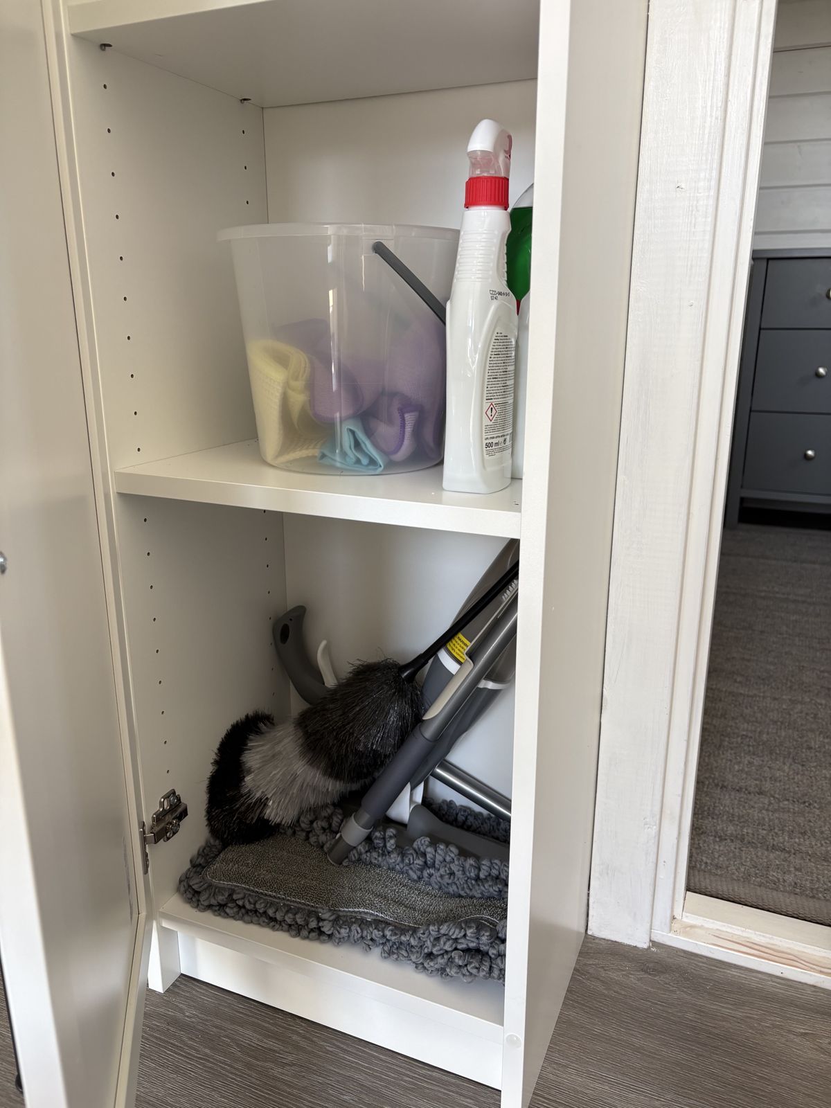 Städskåpet under trappan med dukar, rengöringsmedel, dammvippa och mopp.